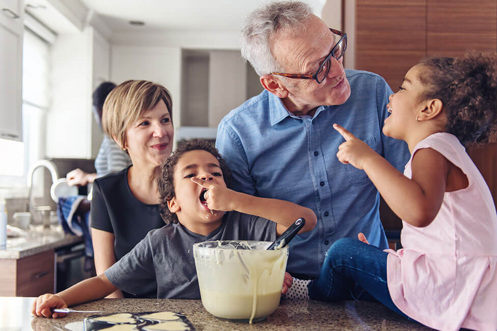 caucasian grandpa and grandma helping their mixed race granchildren bake