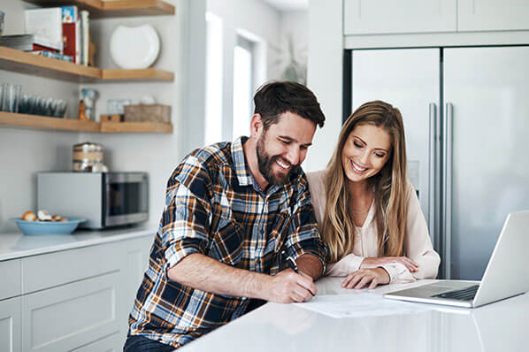 young couple chatting at the kitchen counter looking at papers and laptop